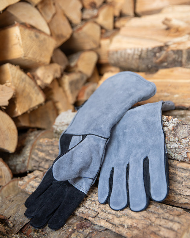 Heath resistant gray leather gloves on a pile of firewood. Used for indoor fireplace, wood stove, or outdoor fire pit, smoker, bbq grill.