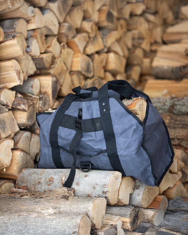 Dark grey waxed canvas firewood carrier filled with logs on top of firewood storage