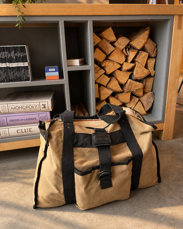 Beige waxed canvas firewood carrier filled with logs beside indoor firewood storage