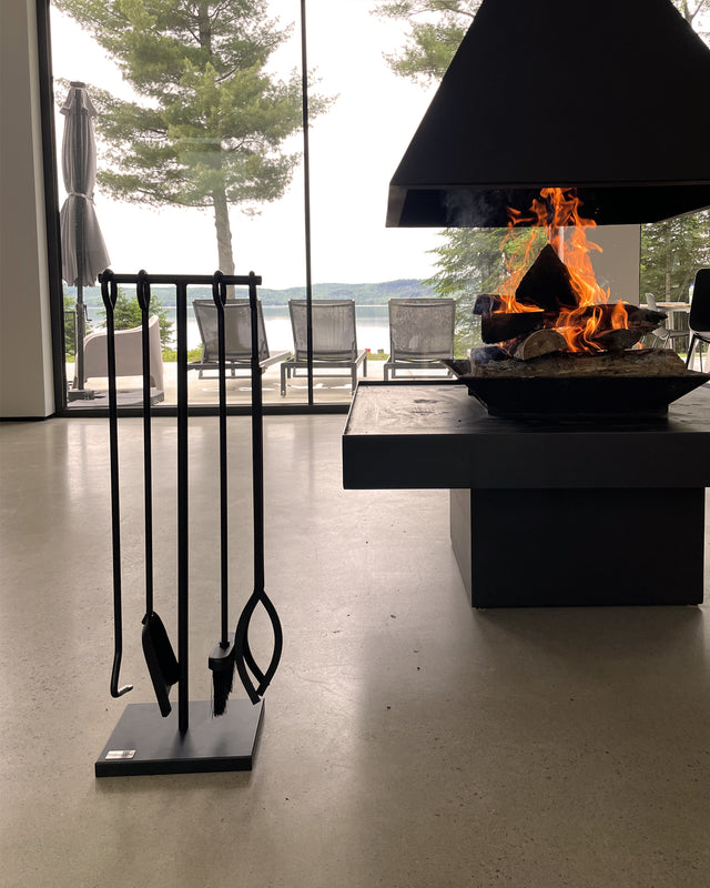 Freestanding Black Iron fireplace tool set beside a four-sided central fireplace in a modern lake house.