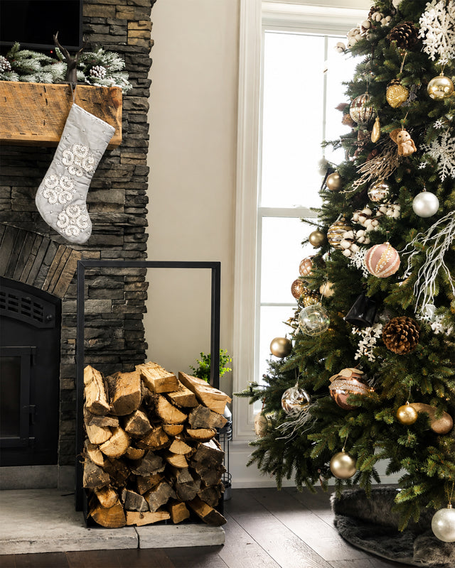 Black Nordic firewood rack filled with logs beside a fireplace in a warm rustic Christmas decor.