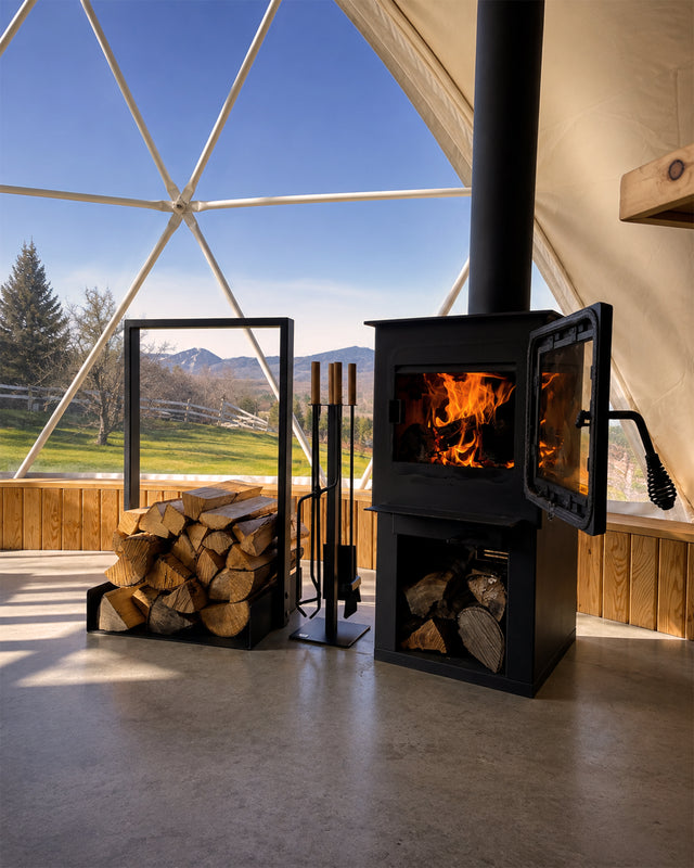 Black Nordic firewood rack beside a wood-burning fireplace with fireplace tools in a cozy cabin interior.