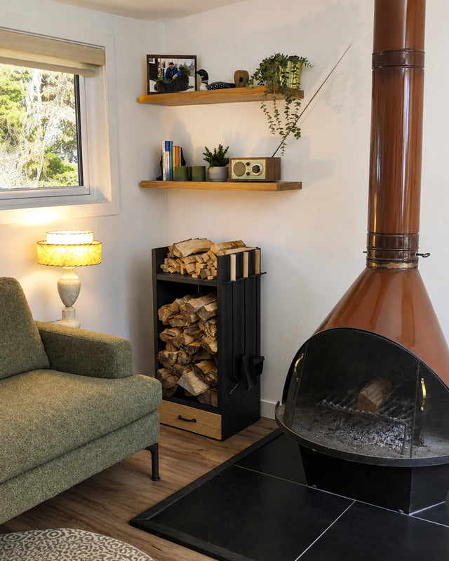 Complete firewood rack filled with logs and kindling, with integrated fireplace tools and wooden drawer beside a midcentury wood-burning fireplace.