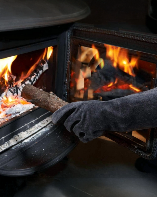 Heat-resistant leather gloves being used to handle firewood in a wood-burning fireplace