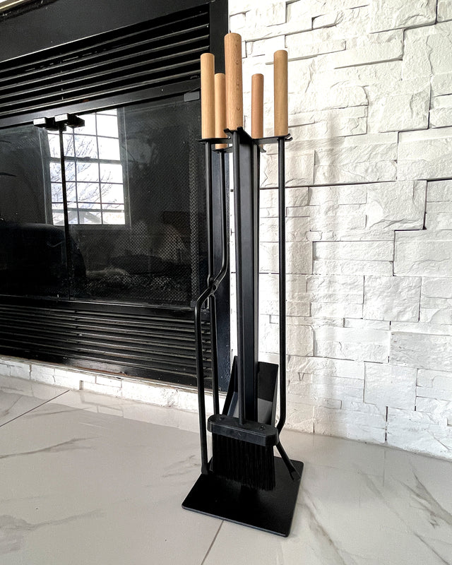 Modern black fireplace tool set with wooden handles placed beside a contemporary wood-burning fireplace.
