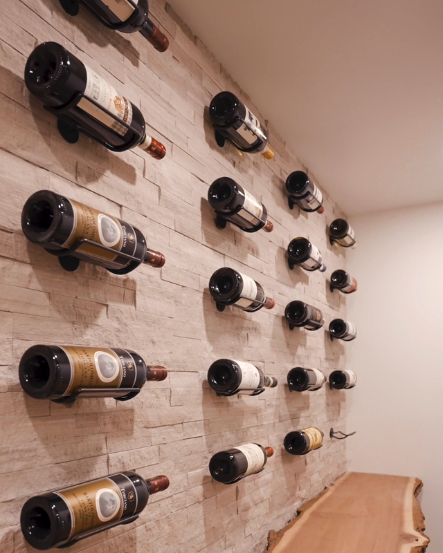 Individual wall mounted wine rack for 1 bottle installed on light stone wall in home wine cellar.