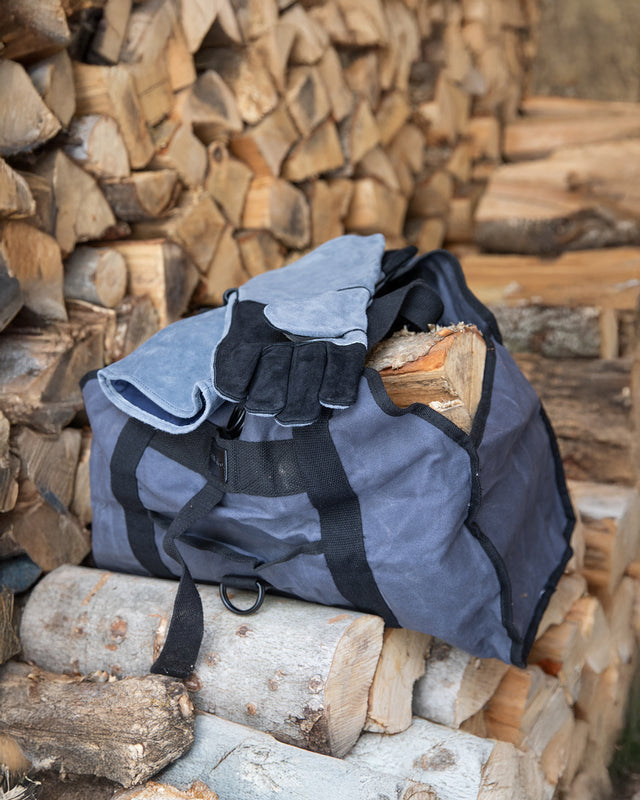 Firewood carrier bag from the Take-Out Kit filled with logs beside stacked firewood