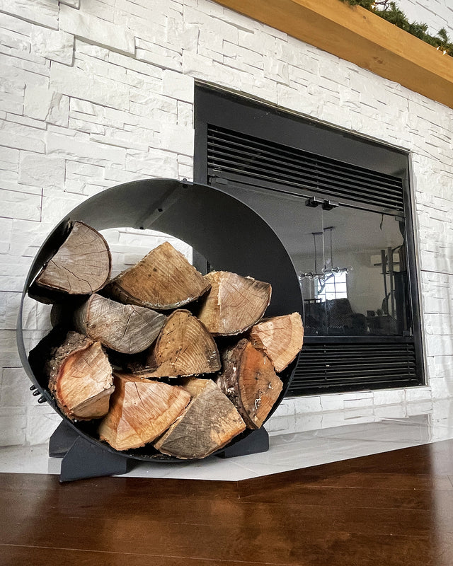Circular firewood rack filled with logs beside a white modern indoor fireplace
