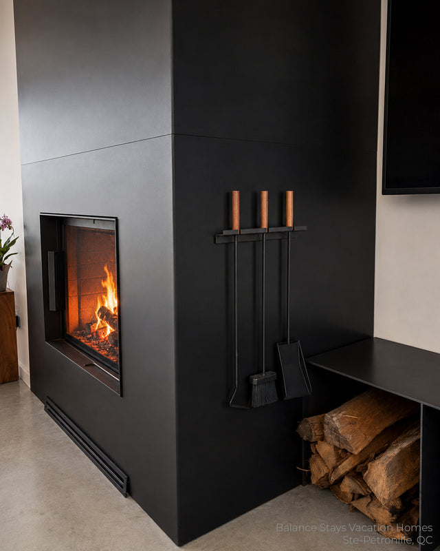 Wall-mounted fireplace tools with wooden handles installed beside a contemporary wood-burning fireplace.