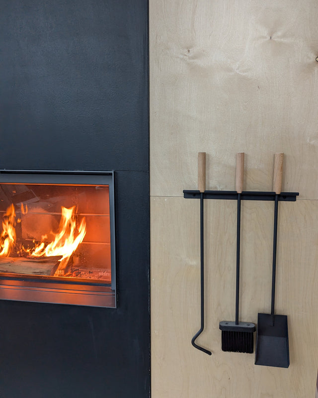 3-piece wall-mounted fireplace tool set installed on a light wood panel beside a modern fireplace.